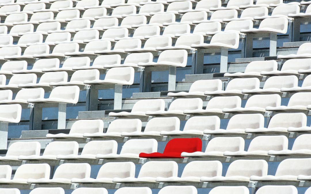 Skats uz sporta stadiona skatītāju zonu - daudz baltu krēslu neskaitāmās rindās. Starp tiem viens krēsls izceļas īpaši, jo ir sarkanā krāsā.